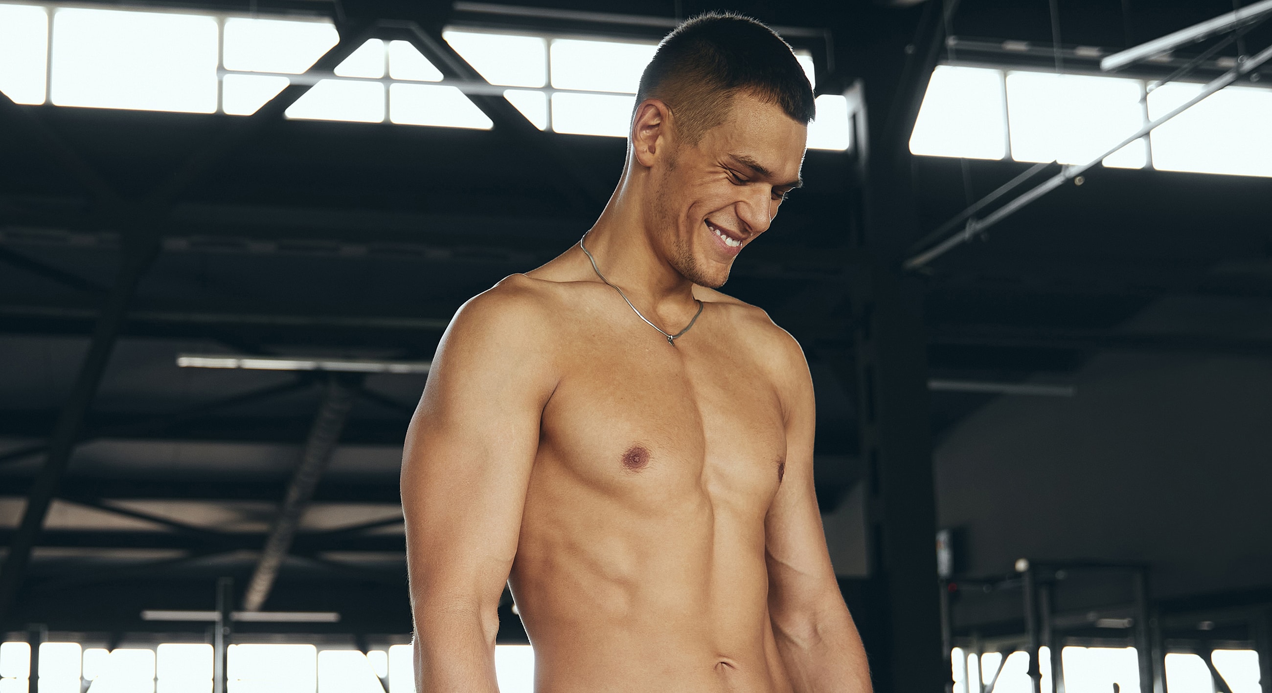 Smiling man in gym, shirtless, confident pose.