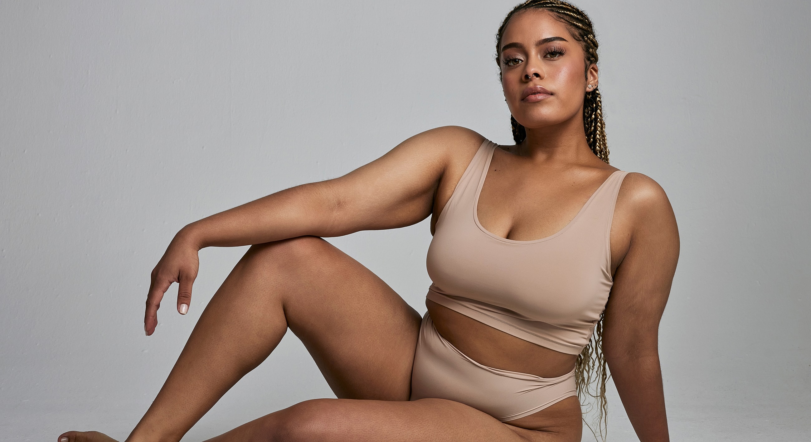 Model posing in beige activewear on neutral background.