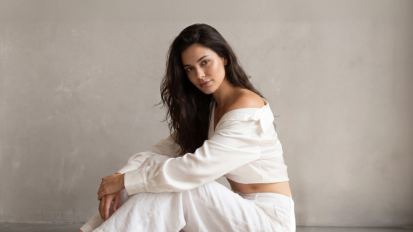 Woman in casual attire, seated against wall.